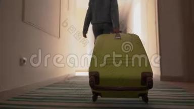 一个年轻的女孩带着一个手提箱沿着酒店走廊走。 入住酒店.. 从后面看。 4k决议